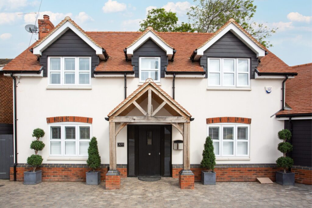 A modern UK detached home with clean brickwork, symmetrical potted plants, and a tidy entrance, showing strong kerb appeal and ideal home presentation.