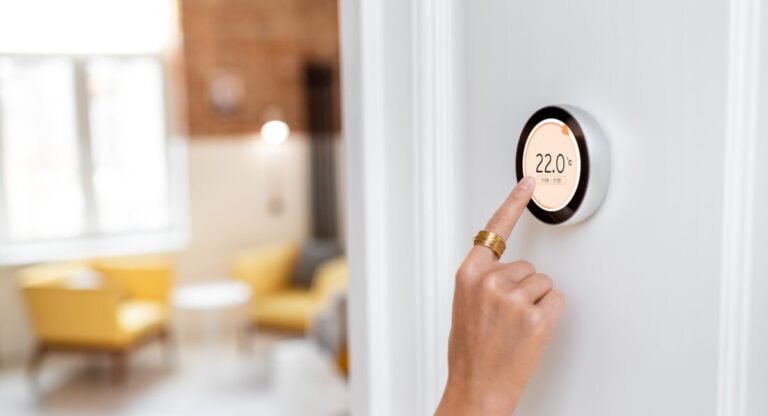Hand turning up a digital smart thermostat on the wall inside a cosy rental home