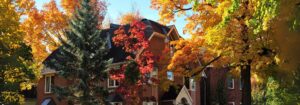 Front view of a brick house surrounded by vibrant autumn trees with red, orange, and yellow leaves