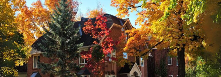 Front view of a brick house surrounded by vibrant autumn trees with red, orange, and yellow leaves