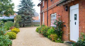 A well-maintained red-brick house with a tidy gravel driveway and blooming garden, representing Country Properties’ professional approach to landlord lease renewals and rent reviews.