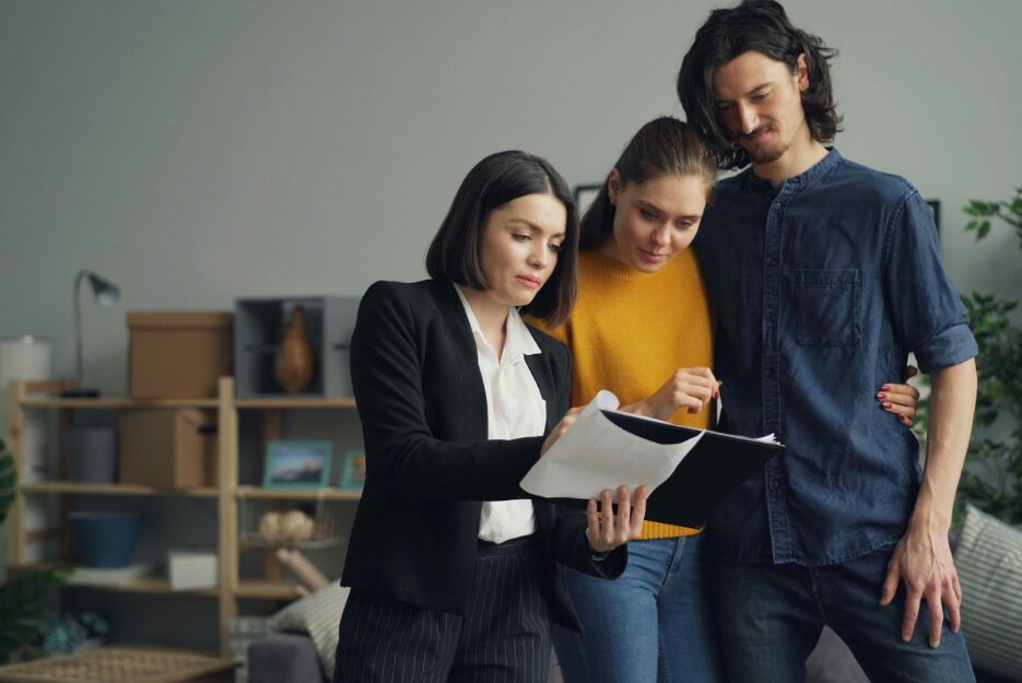 Couple discussing tenancy paperwork with an agent, illustrating self-managing landlords preparing for council compliance checks from 27 December 2025.