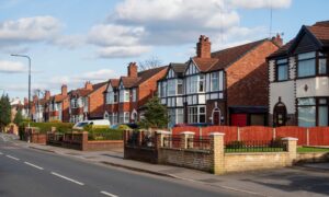 Row of traditional red-brick semi-detached houses with bays, front gardens and driveways along a quiet UK residential road.