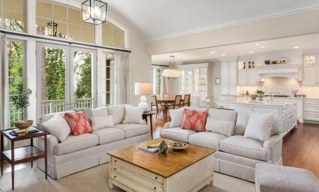 Spacious open-plan living room with large sofas, natural light, and a modern white kitchen in a well-presented home.