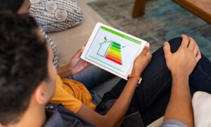 Person holding a tablet displaying a home energy efficiency rating chart while sitting on a sofa.