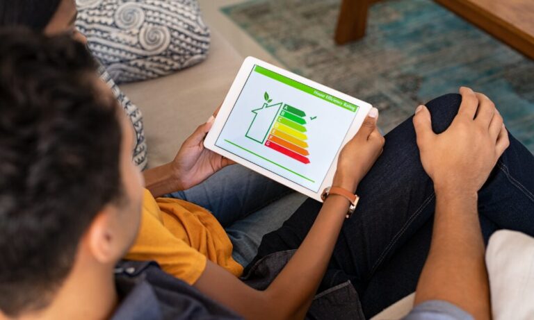 Person holding a tablet displaying a home energy efficiency rating chart while sitting on a sofa.