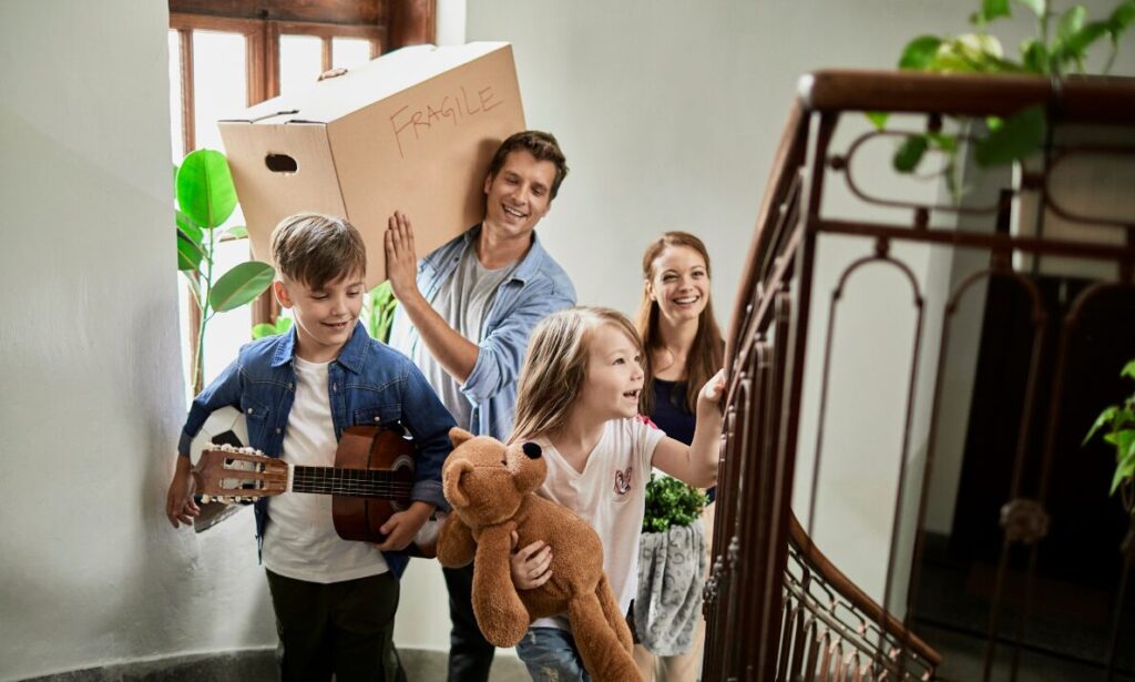 Happy family walking up stairs carrying belongings while moving into a new home.