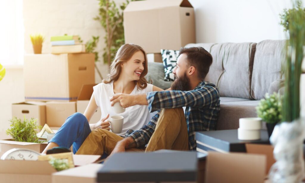 A smiling couple sitting among moving boxes in their new home, representing buyers and renters settling into the lifestyle of living in Biggleswade SG18.