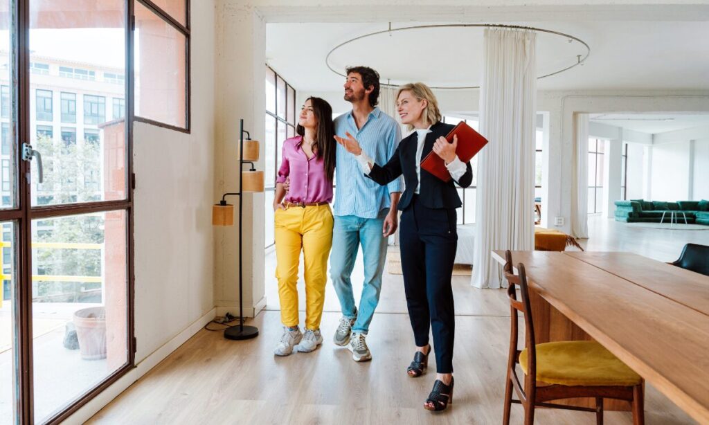 A property agent showing a couple around a bright modern home, representing buyers exploring homes and lifestyle options while living in Hitchin SG5.