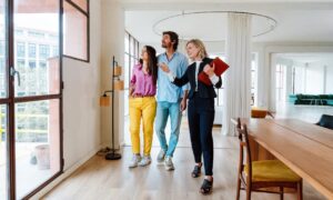 A property agent showing a couple around a bright modern home, representing buyers exploring homes and lifestyle options while living in Hitchin SG5.