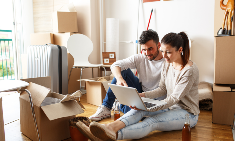 Couple using a laptop while surrounded by moving boxes as they prepare to sell their home.